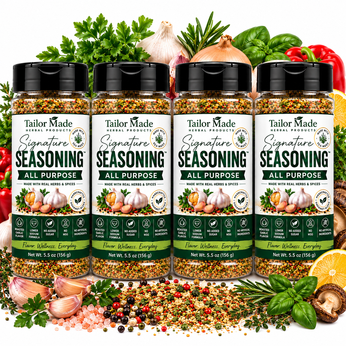 Four bottles of Tailor Made Seasoning All Purpose spice mix arranged in a row, surrounded by fresh herbs, garlic, onions, peppers, and citrus slices on a white background.